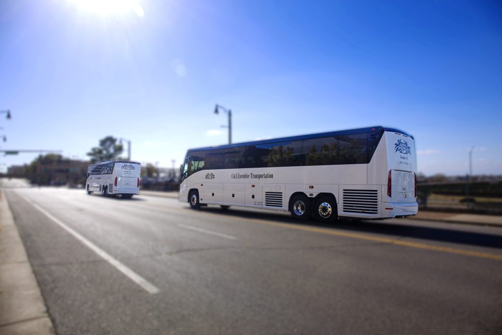 Two C & L Executive Transportation charter buses driving down the road under bright sunlight.